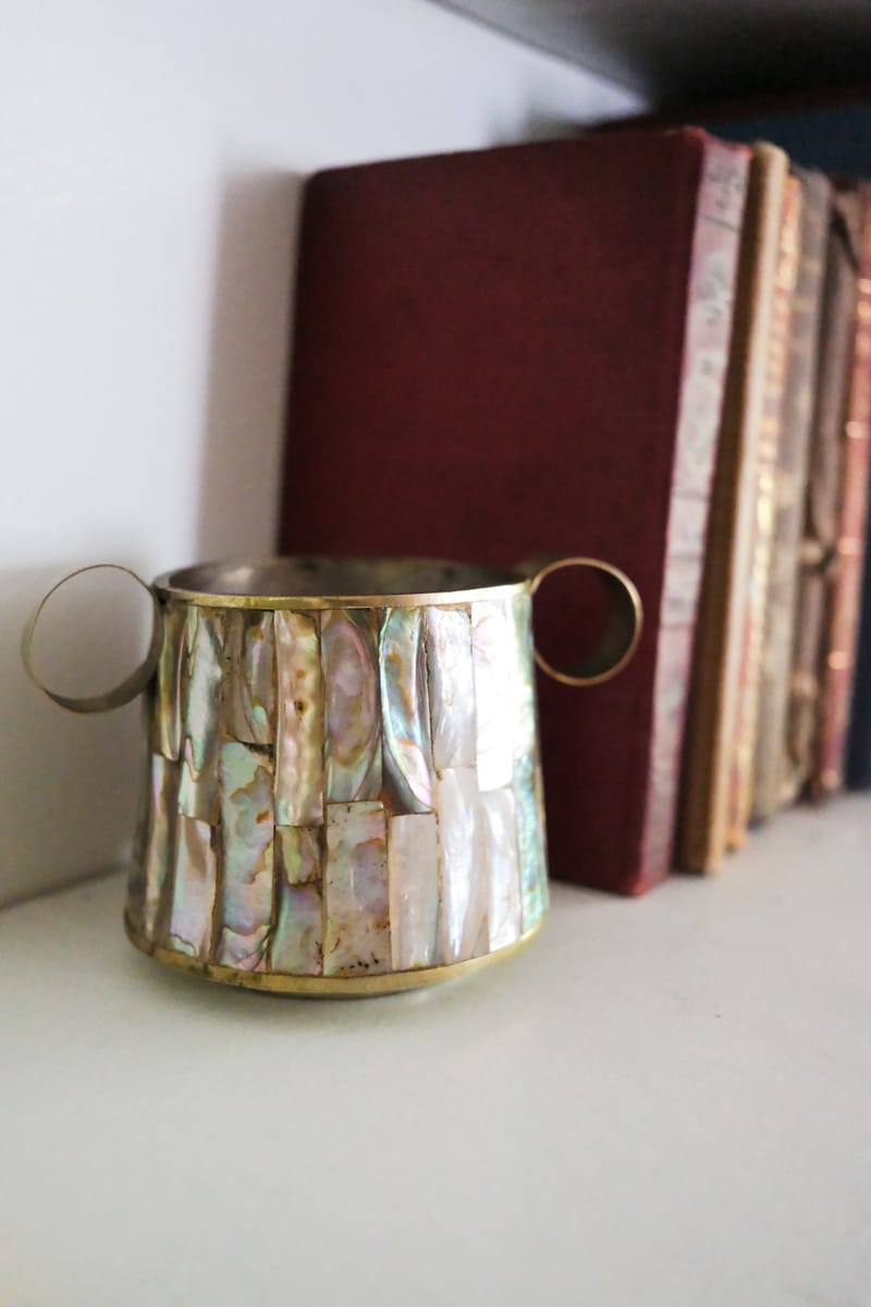 A brass and abalone vessel with looped handles, beside a row of antique leather-bound books