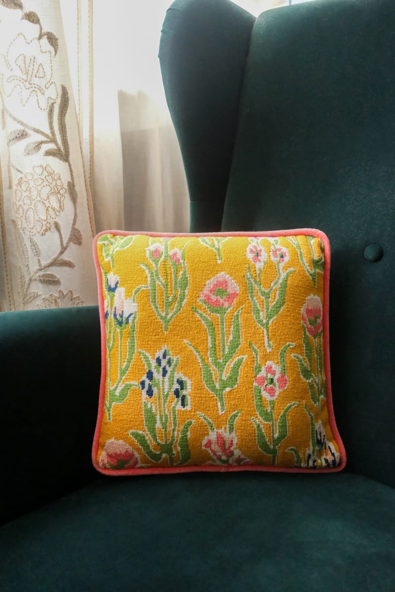 A yellow needlepoint cushion embroidered with tulips and carnations, on a teal velvet armchair